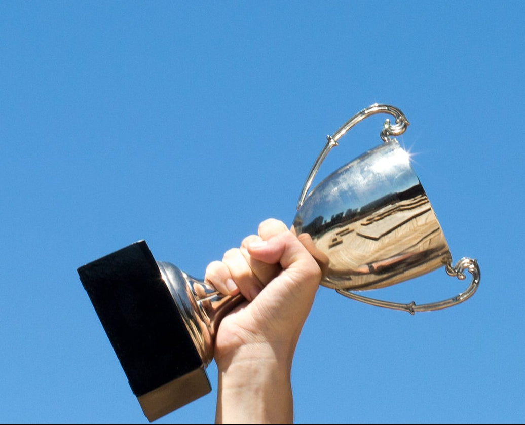 Hand holding a silver trophy against a clear blue sky